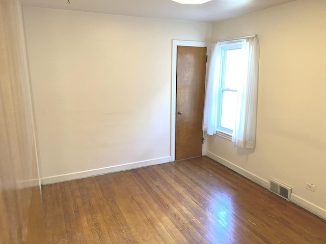 unfurnished room with wood finished floors, visible vents, and baseboards