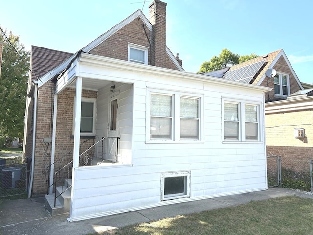 view of property exterior featuring a chimney, central AC, and brick siding