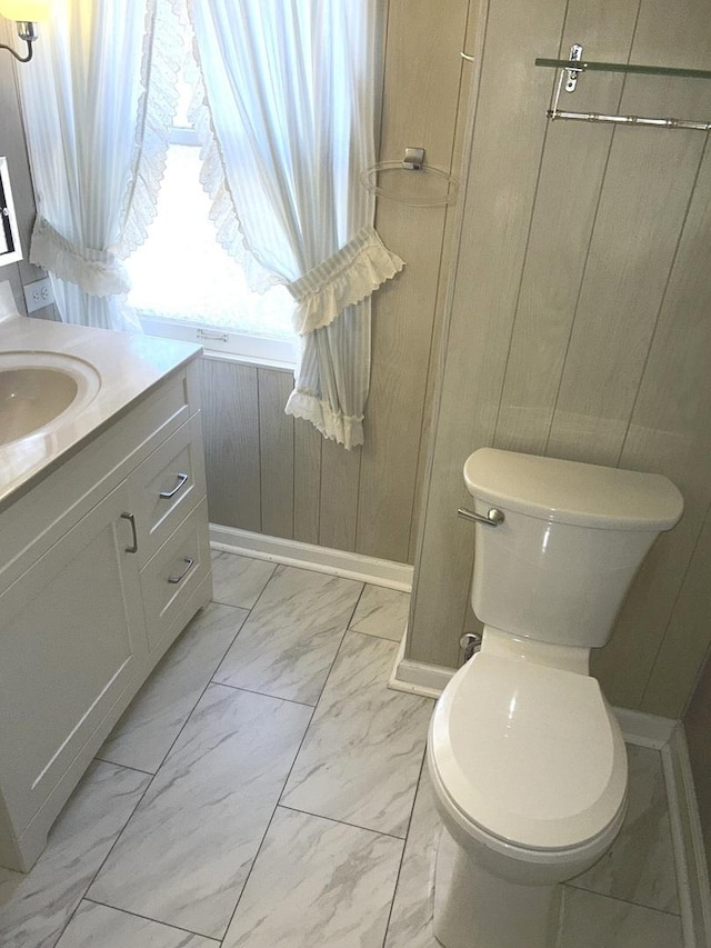 bathroom featuring toilet, wood walls, vanity, baseboards, and marble finish floor