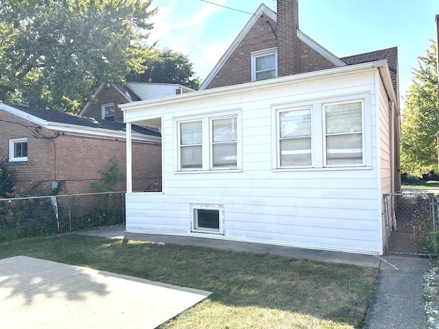 rear view of property featuring brick siding, a chimney, fence, and a lawn