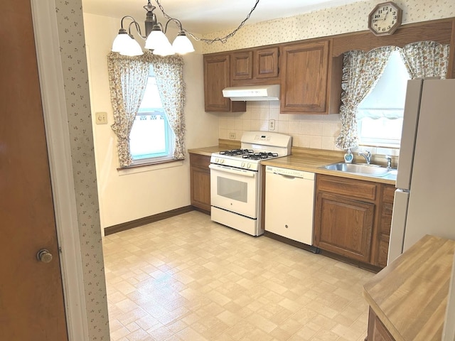 kitchen featuring a notable chandelier, under cabinet range hood, white appliances, a sink, and light countertops