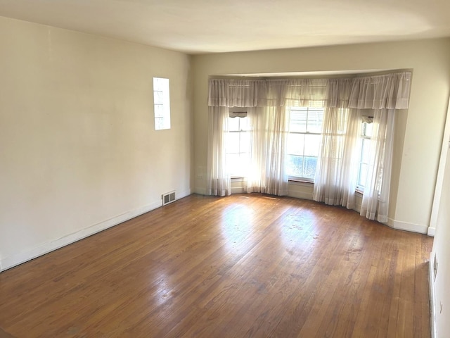 empty room featuring wood-type flooring, visible vents, and baseboards