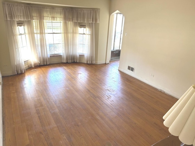 spare room featuring arched walkways, visible vents, baseboards, and wood finished floors