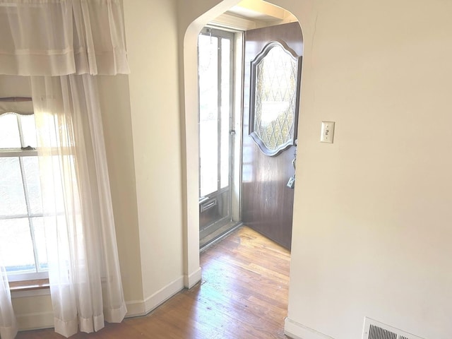 hall featuring arched walkways, wood finished floors, visible vents, and baseboards