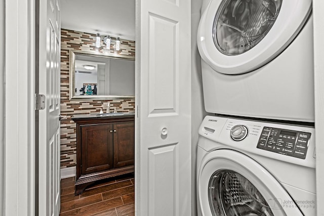 laundry area featuring laundry area, wood finish floors, a sink, and stacked washer and clothes dryer