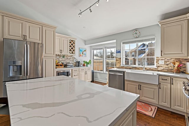 kitchen featuring light stone countertops, appliances with stainless steel finishes, vaulted ceiling, and a sink