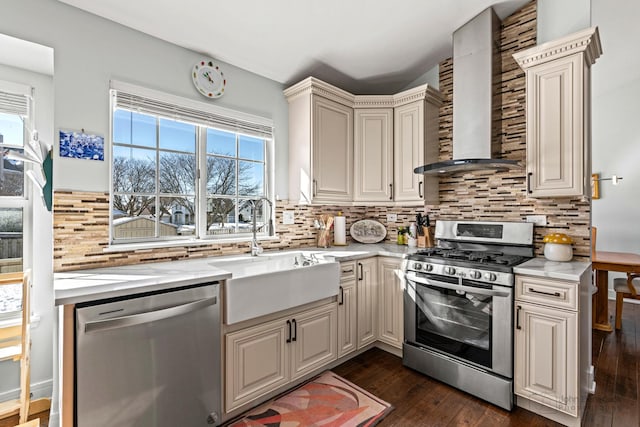 kitchen featuring decorative backsplash, dark wood-style floors, appliances with stainless steel finishes, wall chimney range hood, and a sink