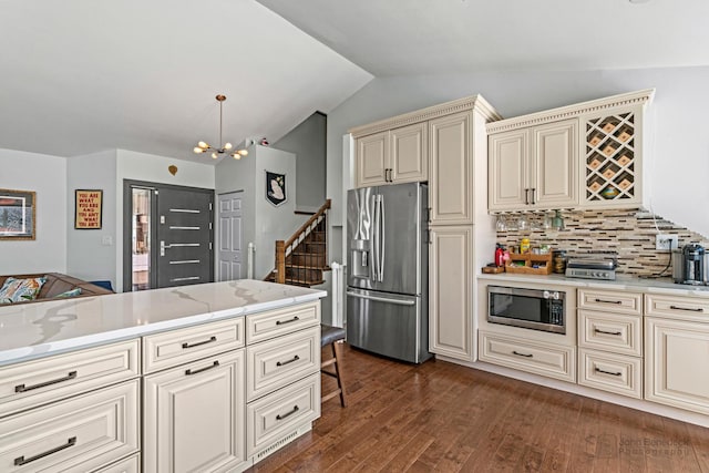 kitchen with stainless steel appliances, vaulted ceiling, cream cabinetry, dark wood-style floors, and decorative light fixtures