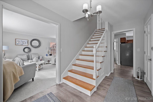 stairs with an inviting chandelier, baseboards, and wood finished floors