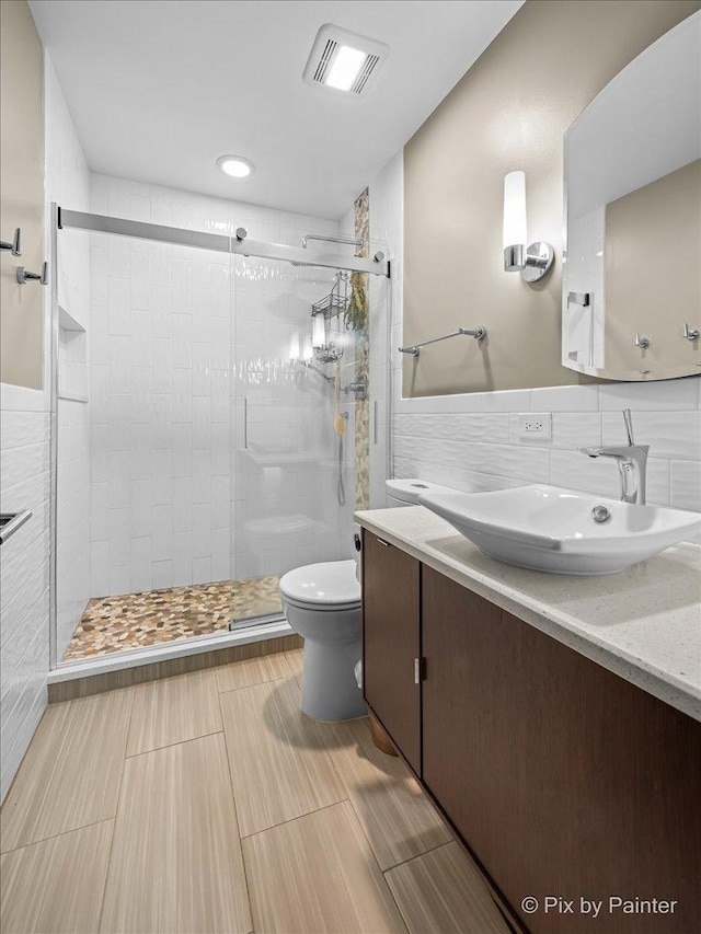 full bathroom with visible vents, a shower stall, toilet, tile walls, and vanity