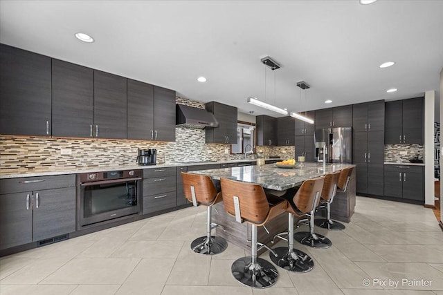 kitchen featuring a breakfast bar, a kitchen island, pendant lighting, stainless steel appliances, and wall chimney range hood