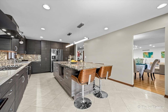 kitchen with hanging light fixtures, a center island with sink, appliances with stainless steel finishes, backsplash, and a kitchen bar