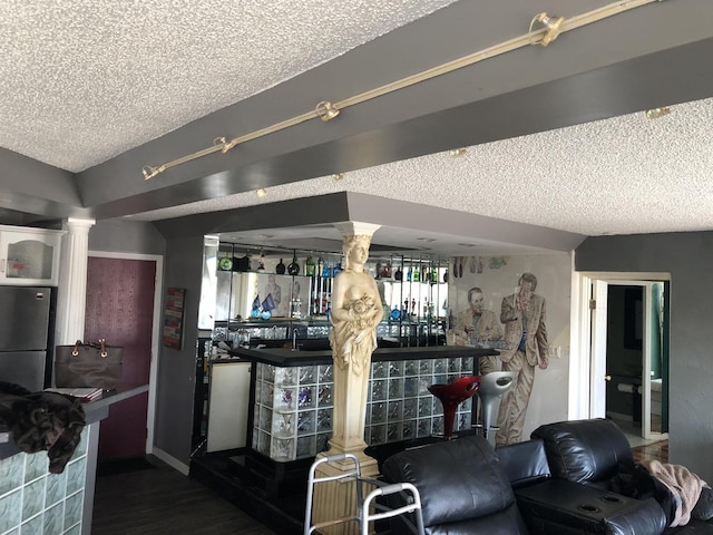 interior space featuring stainless steel refrigerator, ornate columns, dark wood-type flooring, and a textured ceiling