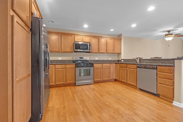 kitchen with light hardwood / wood-style flooring, ceiling fan, appliances with stainless steel finishes, kitchen peninsula, and dark stone counters