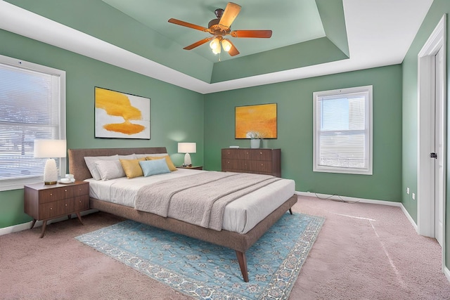 bedroom with light colored carpet, ceiling fan, and a tray ceiling