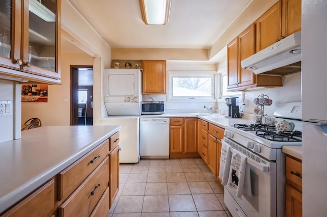 kitchen with stacked washer and dryer, white appliances, sink, and light tile patterned floors