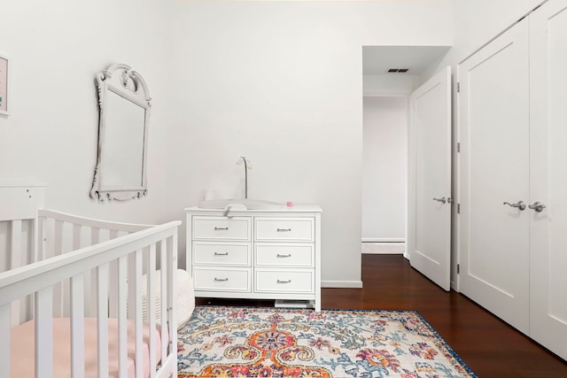 bedroom with a crib, dark hardwood / wood-style floors, and a closet