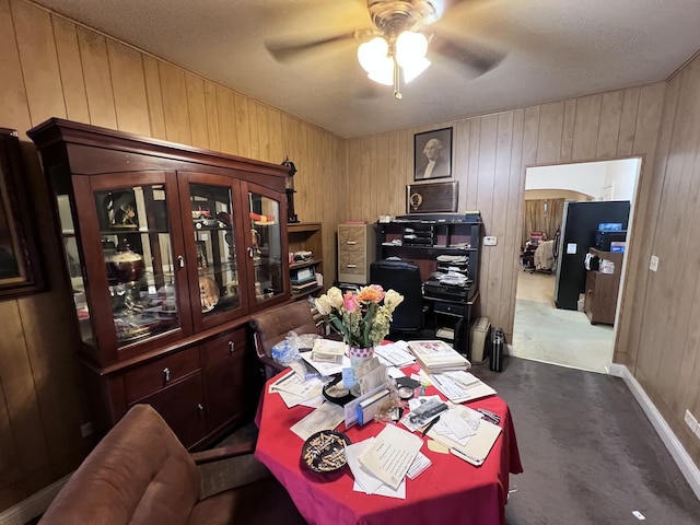 carpeted office featuring ceiling fan and wood walls