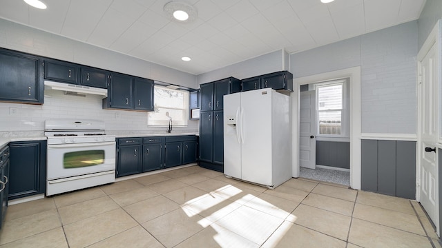 kitchen with blue cabinetry, white appliances, a wealth of natural light, and light tile patterned floors