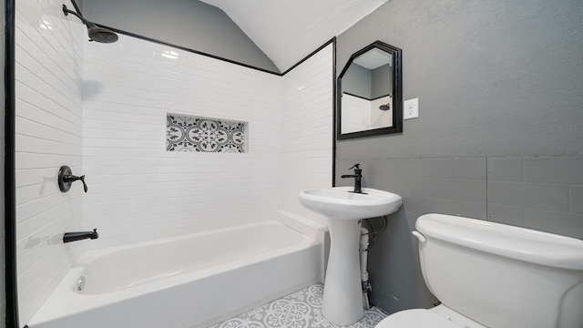 bathroom featuring tiled shower / bath combo, vaulted ceiling, tile walls, and toilet