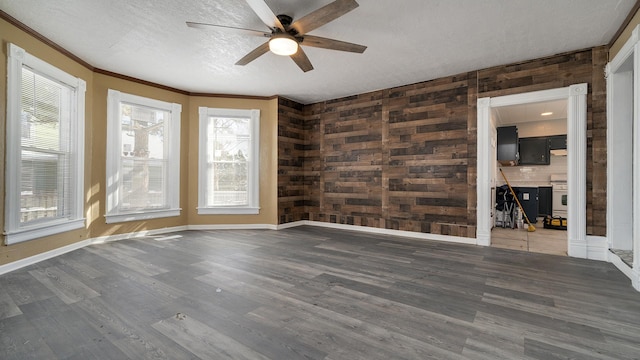 empty room featuring wood walls, ceiling fan, crown molding, dark wood-type flooring, and a textured ceiling