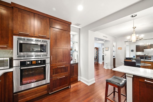 kitchen featuring stainless steel appliances, visible vents, light stone countertops, dark wood-style floors, and decorative light fixtures