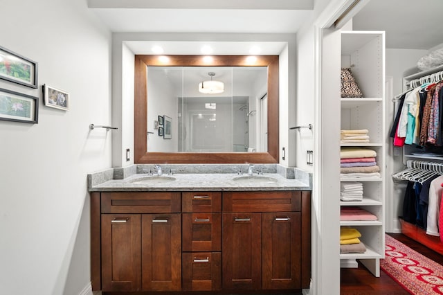 bathroom featuring double vanity, a stall shower, a walk in closet, and a sink