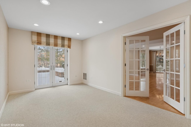 carpeted spare room with a notable chandelier and french doors