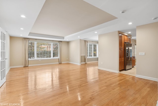 unfurnished living room featuring a raised ceiling and light hardwood / wood-style floors