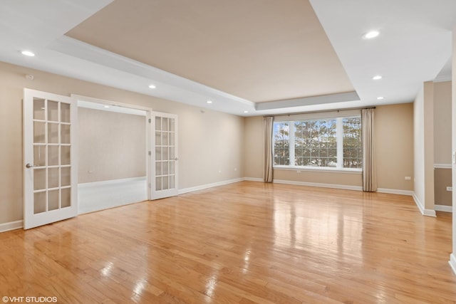 unfurnished room featuring a raised ceiling, light hardwood / wood-style flooring, and french doors