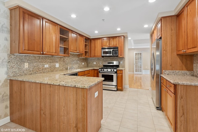 kitchen featuring stainless steel appliances, sink, light stone counters, and kitchen peninsula