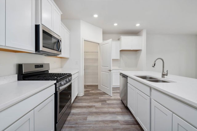 kitchen with appliances with stainless steel finishes, sink, white cabinetry, and light hardwood / wood-style floors