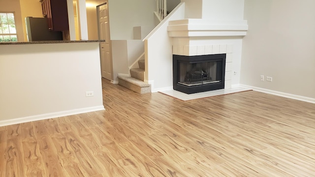 unfurnished living room featuring a tiled fireplace and light wood-type flooring