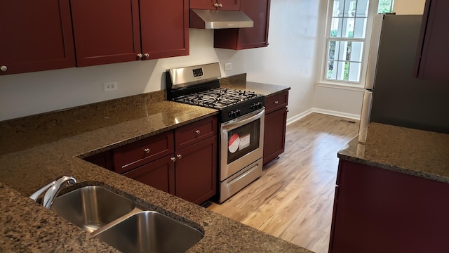 kitchen with dark stone countertops, sink, light wood-type flooring, and appliances with stainless steel finishes