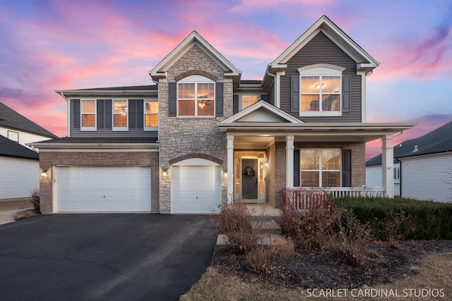 traditional-style home with aphalt driveway, a garage, covered porch, brick siding, and stone siding