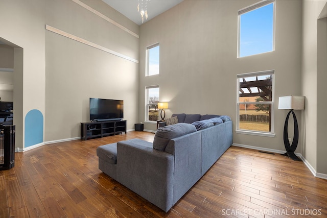 living area featuring dark wood-type flooring, a towering ceiling, and baseboards