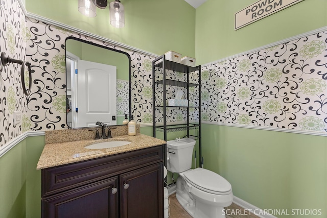 half bathroom featuring toilet, baseboards, and vanity