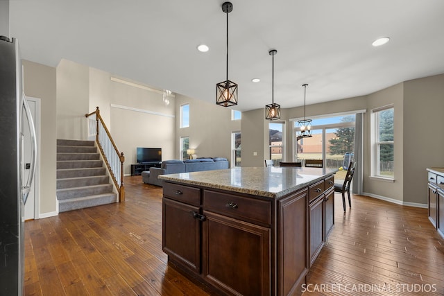 kitchen featuring light stone counters, dark wood-type flooring, dark brown cabinets, freestanding refrigerator, and pendant lighting