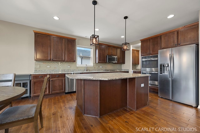 kitchen featuring a sink, appliances with stainless steel finishes, a center island, dark wood-style floors, and tasteful backsplash