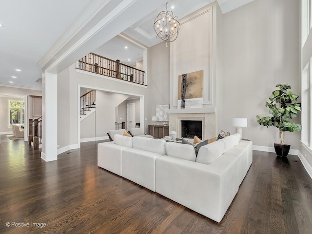 living room featuring a chandelier, crown molding, a high ceiling, a premium fireplace, and dark wood-type flooring