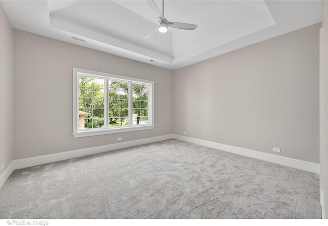 carpeted empty room with a raised ceiling and ceiling fan