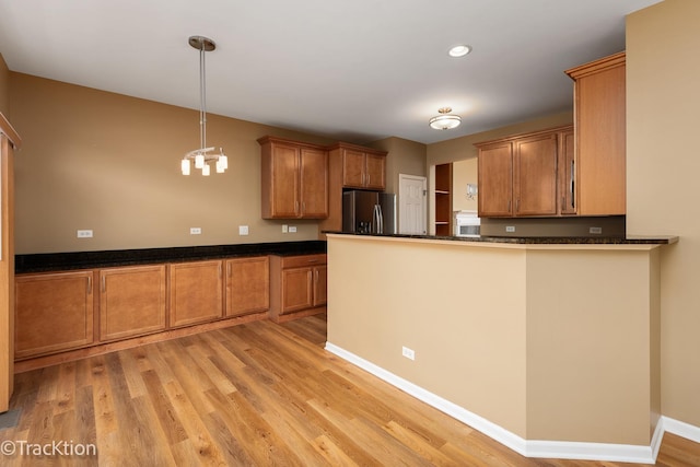 kitchen featuring pendant lighting, kitchen peninsula, stainless steel fridge with ice dispenser, and light wood-type flooring