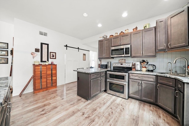 kitchen with sink, dark brown cabinets, stainless steel appliances, light stone counters, and a barn door