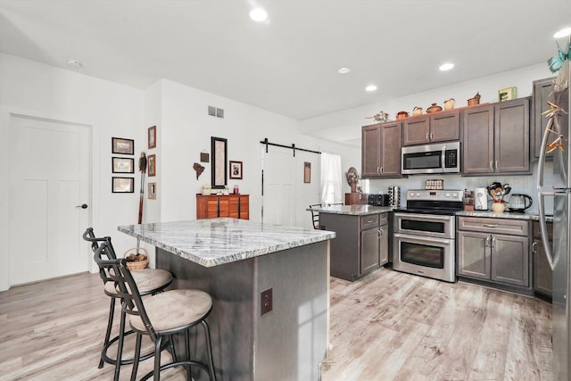 kitchen featuring dark brown cabinetry, appliances with stainless steel finishes, a kitchen island, a barn door, and light stone countertops