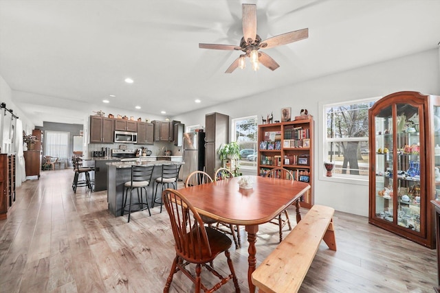 dining room with light hardwood / wood-style flooring, a barn door, and ceiling fan