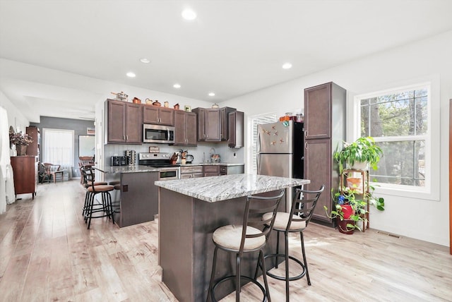 kitchen with light wood-type flooring, a kitchen island, a kitchen breakfast bar, and appliances with stainless steel finishes