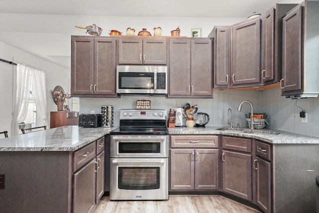 kitchen with sink, dark brown cabinets, stainless steel appliances, light stone counters, and light wood-type flooring