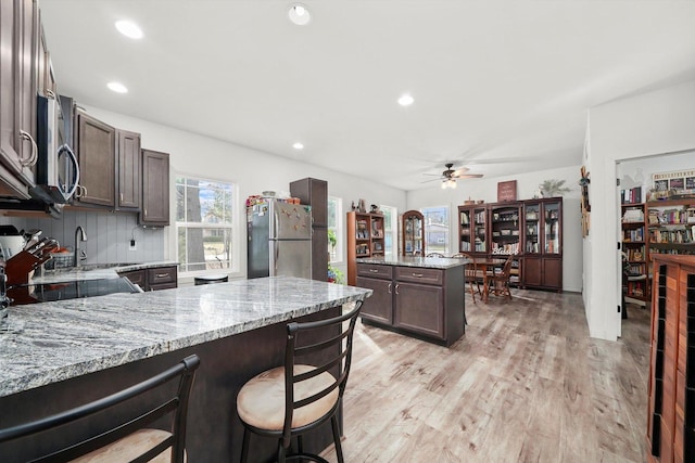 kitchen featuring light stone counters, light wood-type flooring, stainless steel appliances, and a kitchen bar