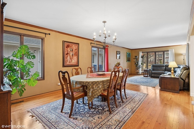 dining area with visible vents, crown molding, light wood finished floors, and an inviting chandelier