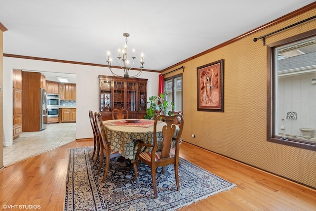 dining room featuring an inviting chandelier, crown molding, wallpapered walls, and light wood-style floors